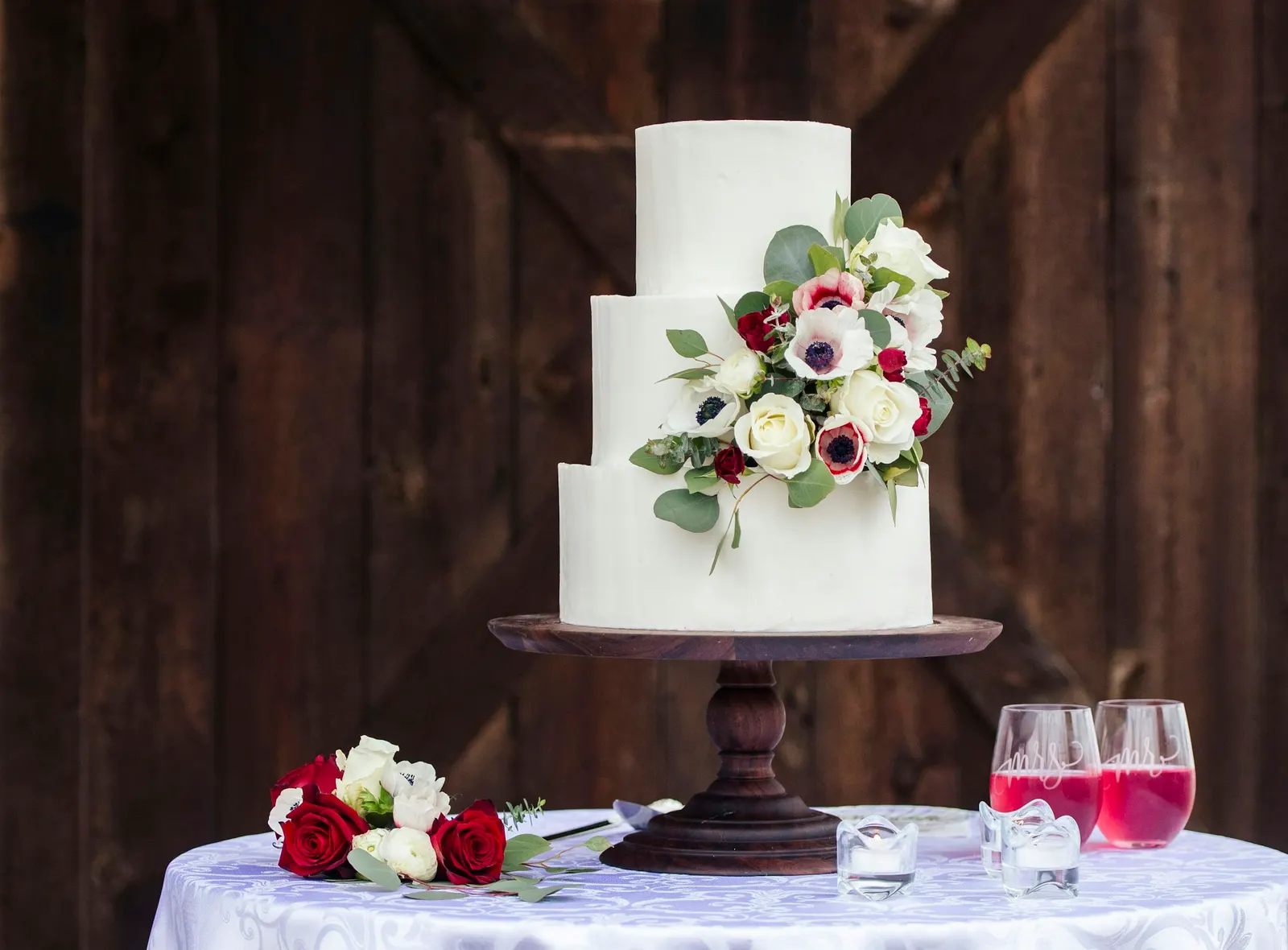 Dreistöckige weiße Festtorte mit Blumenschmuck vor einer dunklen Holzwand