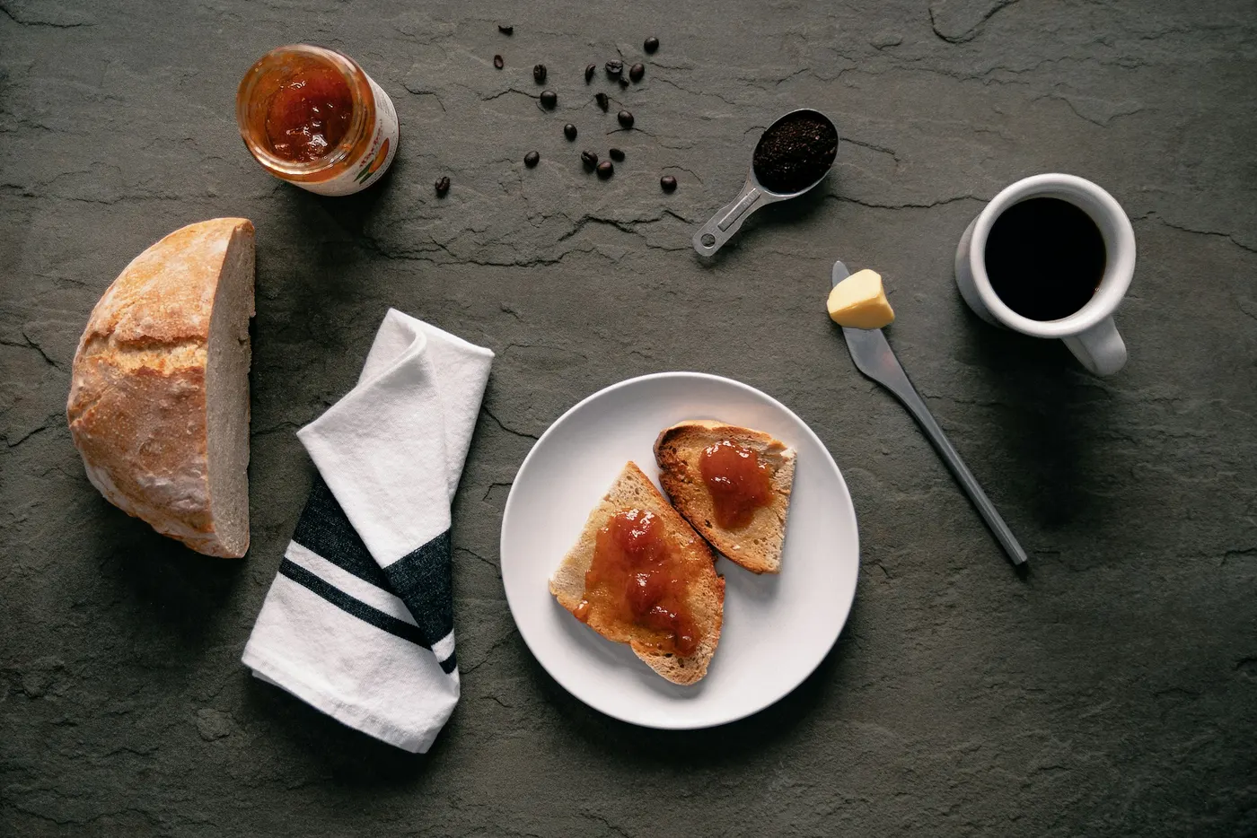 Frühstück von oben: angeschnittenes Brot, Marmeladebrote auf einem Teller und eine Tasse Kaffee