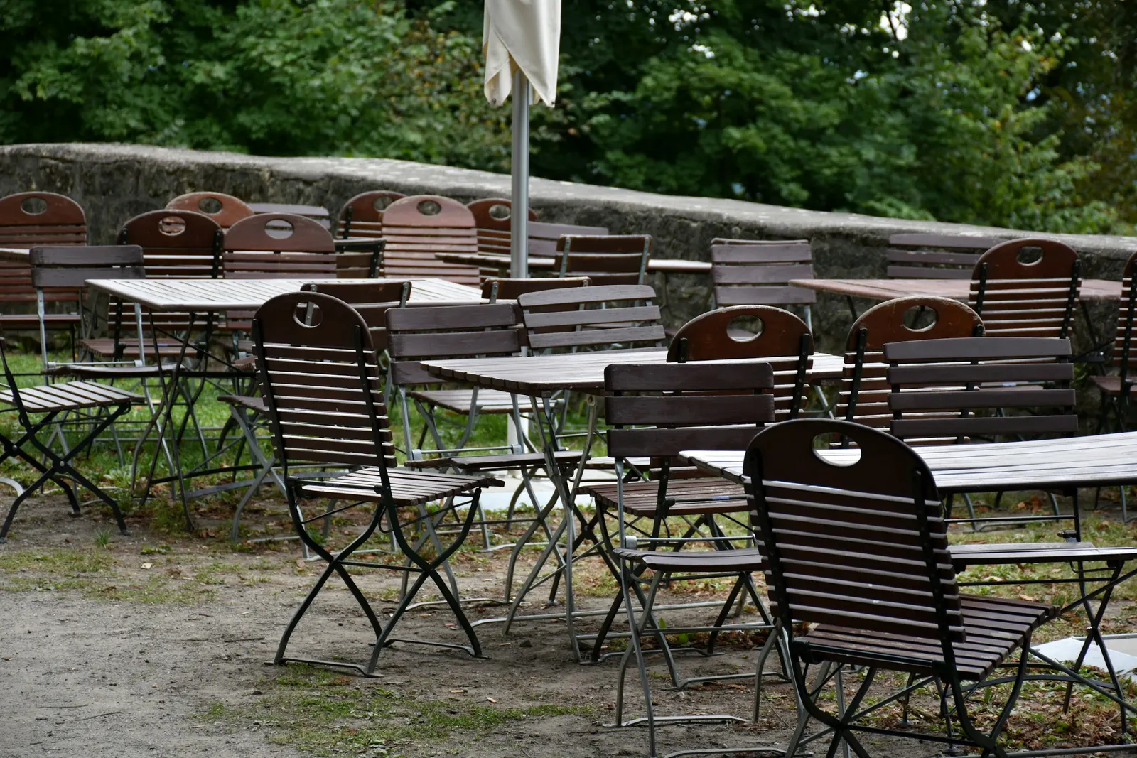 Gastgarten mit Holzklappstühlen und Tischen unter Bäumen