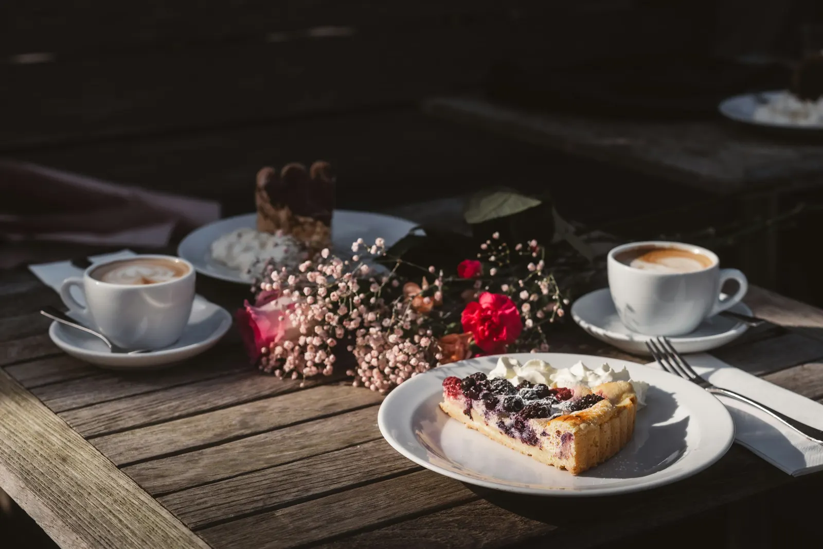 Zwei Tassen Kaffee und ein Stück Beerenkuchen auf einem Holztisch im Freien