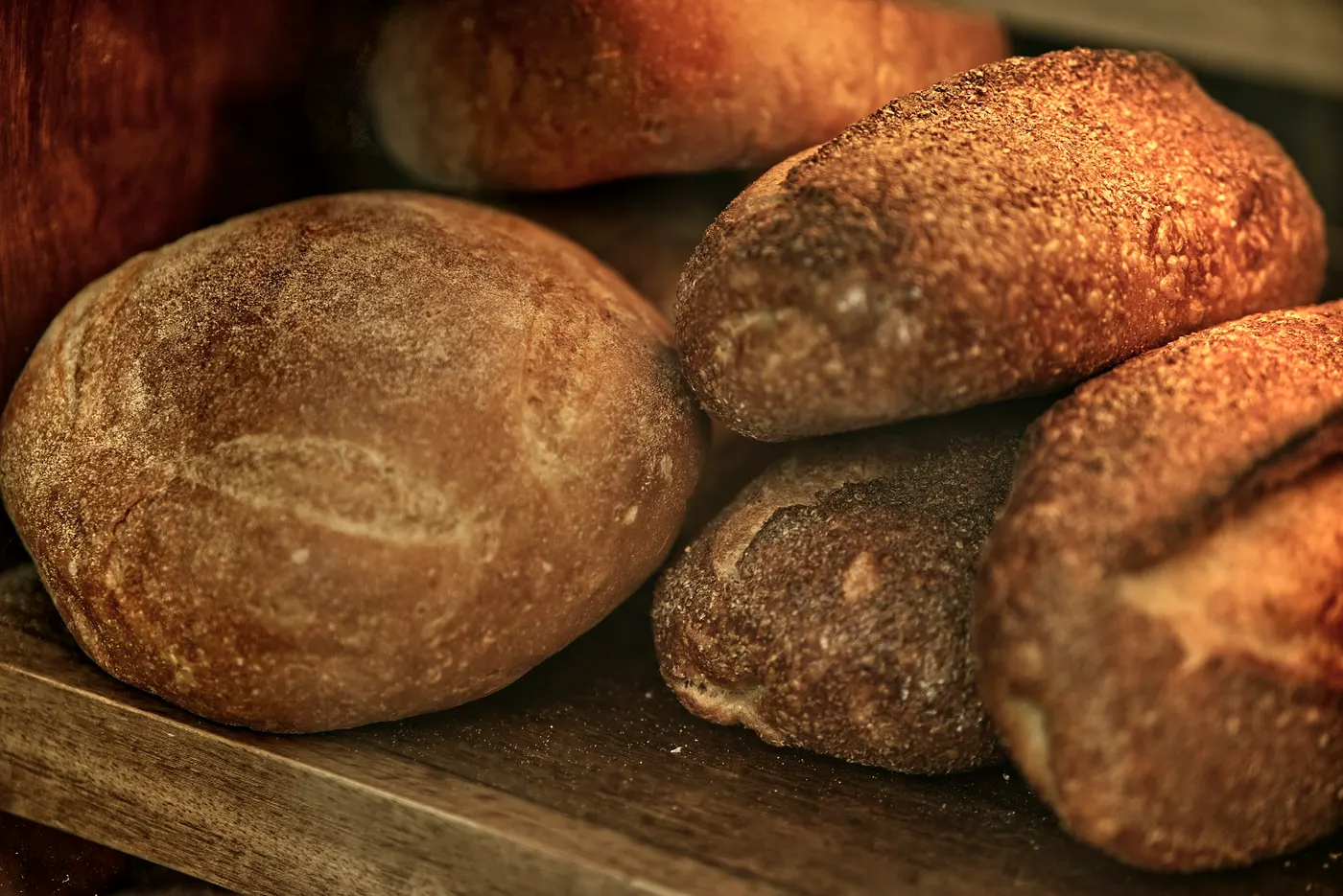 Rustikale, dunkel gebackene Weckerl, übereinander auf einem Holzbrett gestapelt